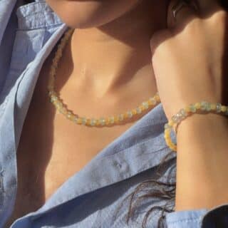 try-on shot of the hand-beaded Citrine Skies set of necklace and bracelet in butter yellow agate stones and tourmaline blue stones. A soft summer day, captured in stone. Inspired by the golden warmth of citrine sunsets and the tranquility of clear skies. Blends butter yellow and sky blue tones in a dreamy, refreshing palette. Handcrafted with natural jade and tourmaline gemstones and finished with 925 sterling silver clasp. Material: Natural jade stones - Length: 42 cm - 925 sterling silver clasp.