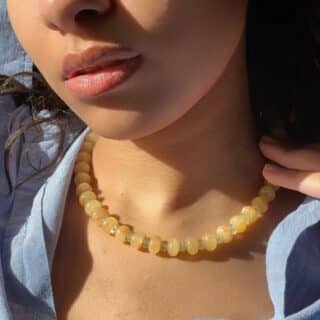 try on shot of the hand-beaded Citrine Skies Necklace No.02 in butter yellow agate stones and tormaline blue stones A soft summer day, captured in stone.Inspired by the golden warmth of citrine sunsets and the tranquility of clear skies. Blends butter yellow and sky blue tones in a dreamy, refreshing palette. Handcrafted with natural jade and tormaline gemstones and finished with 925 sterling silver clasp. Featuring: Material: Natural jade stones - Length: 42 cm - 925 sterling silver clasp